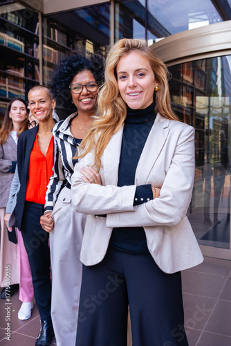 Group of confident businesswomen standing together outdoors in front of modern office building. Leadership, teamwork, empowerment, success and professional diversity concept in business world.