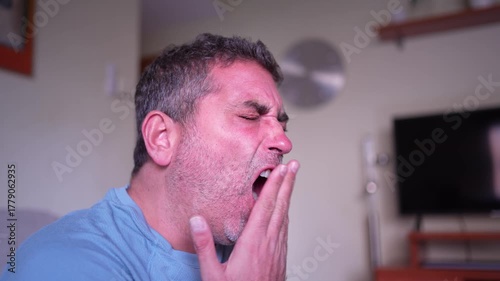 A Man Yawning Expressively While Sitting in a Living Room Setting During the Day