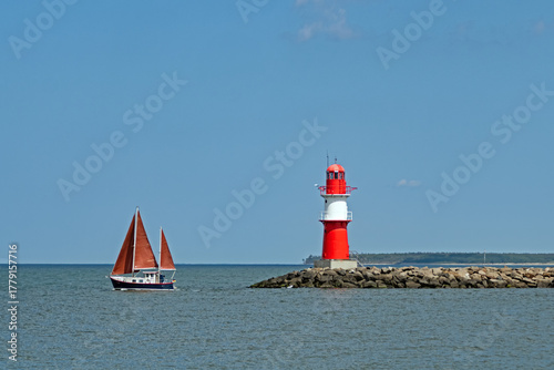 Ein Segelboot kreuzt in der Ostsee vor dem Leuchtturm von Rostock Warnemünde, Deutschland