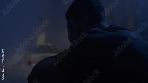 Sad depressed man sitting alone in dark bedroom, emotional burnout, hopeless mood and loneliness.