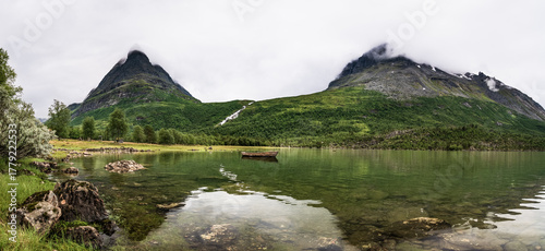 Beautiful Innerdalen valley showcases stunning scenery with a solitary boat floating on Innerdalsvatna lake in Norway. Skardfjell and Innerdalstarnet mountains rise majestically in the background.
