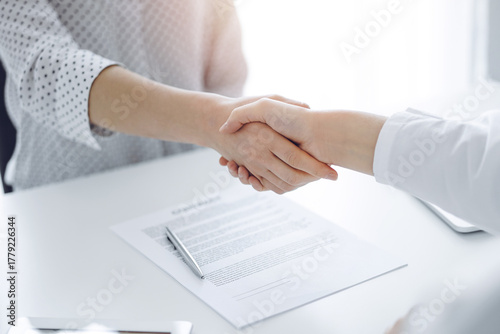 Business people shaking hands above contract papers just signed on the white table, closeup. Lawyers at meeting. Teamwork, partnership, success concept