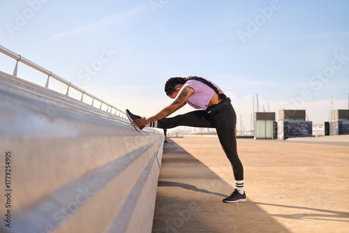Fotografie side view of Hispanic woman stretching leg exercising in urban environment