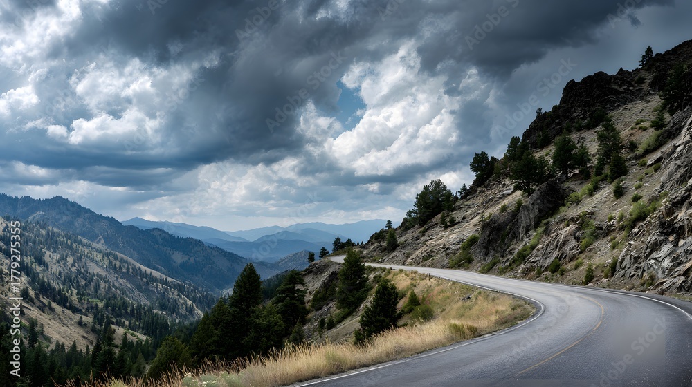 Fototapeta premium Winding paved road curves sharply along a steep, rocky mountainside under dramatic, heavy cloud cover.