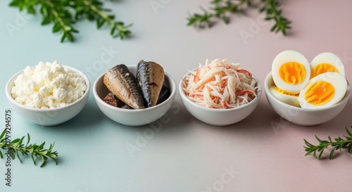 Four bowls of healthy food items including cottage cheese, sardines, crab meat, and boiled eggs, arranged on a pastel background with green herbs.