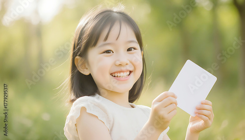 Smiling Asian Girl Holding Blank White Card Outdoors, Ready for Your Message or Design, Promoting Creativity and Joy                                  