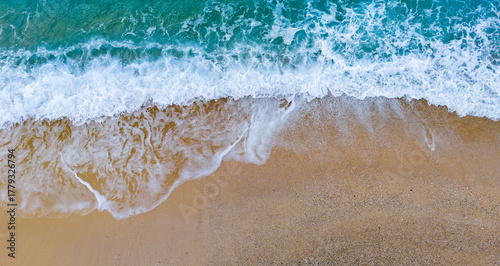 Spectacular high-angle drone video of deep turquoise ocean waves crashing diagonally onto a golden sand beach. Stunning aerial view capturing the dynamic white foam and marine coast textures.