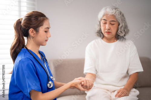 Asian adult nurse offers professional nursing care assessing older woman hand during home visit providing compassionate medical support for senior patient well being