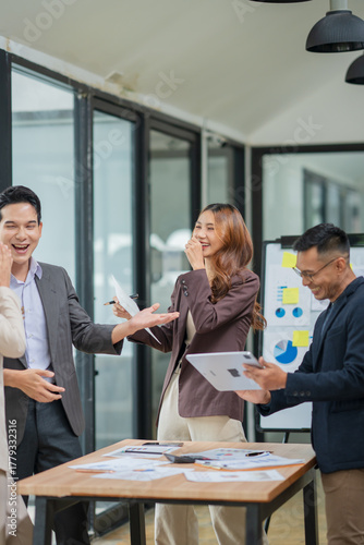 Group of young Asian professionals engaging in a dynamic brainstorming session. A female leader stands confidently while presenting ideas to her colleagues, showcasing a collaborative, positive