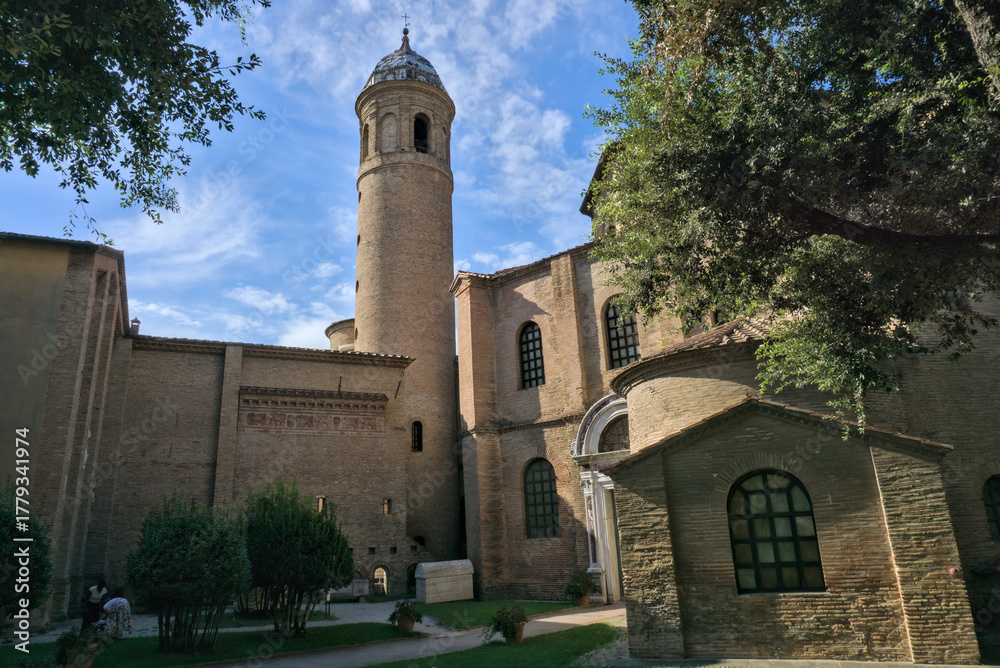 Obraz premium View of a cylindrical bell tower (Campanile) and basilica structure in Ravenna, framed by trees.