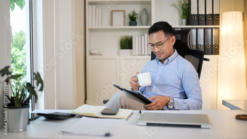 Smiling professional reads on a tablet during a coffee break in a tidy home office.
