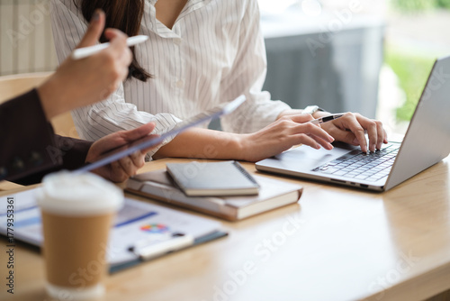 Close-up of hands working on laptop and tablet during a business discussion at a modern desk.