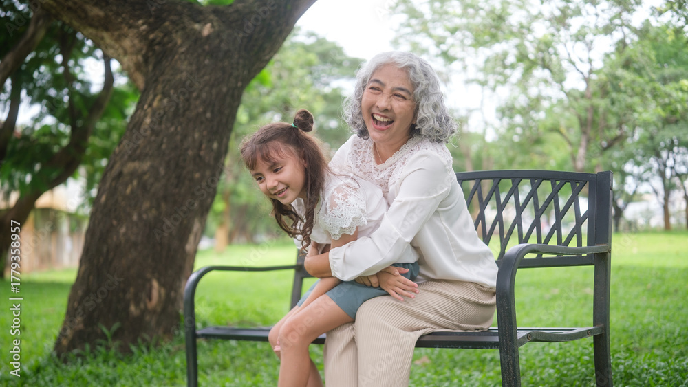 Fototapeta premium Elderly woman embraces young girl in a warm hug while laughing together in a park setting.