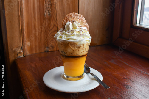 Bombardino - an Italian hot cocktail made with egg liquor (Advocaat) and brandy. Served in a glass mug with fresh whipped cream and a biscuit in an alpine bar in an Italian ski resort.