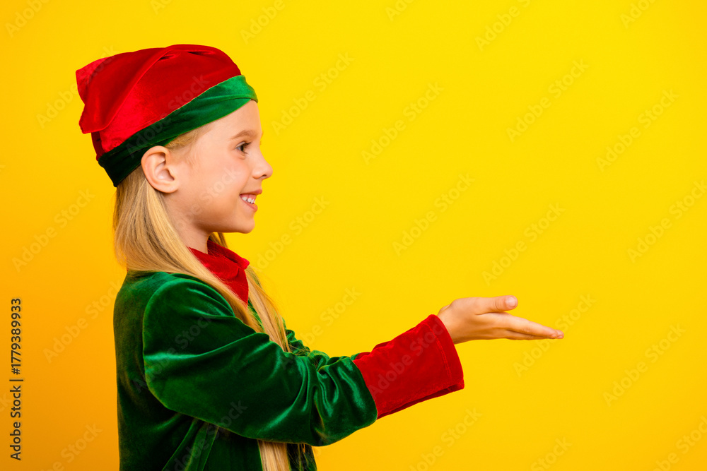 Obraz premium Smiling child in a festive elf costume poses against a vibrant yellow background, ready to spread Christmas cheer and joy