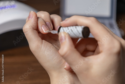 Woman's hands applying clear gel nail polish by oneself, performing a meticulous home manicure, symbolizing self-care and personal grooming
