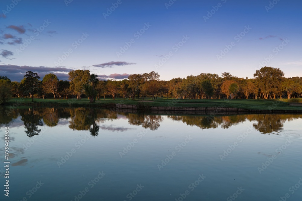 Obraz premium Serene lake scene at sunset with reflections of trees and a calm sky creating a peaceful atmosphere