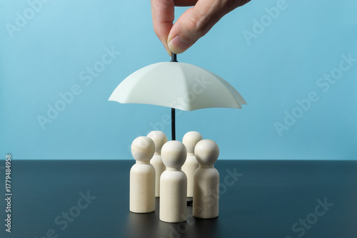Wooden doll figures with toy umbrella. Insurance coverage concept