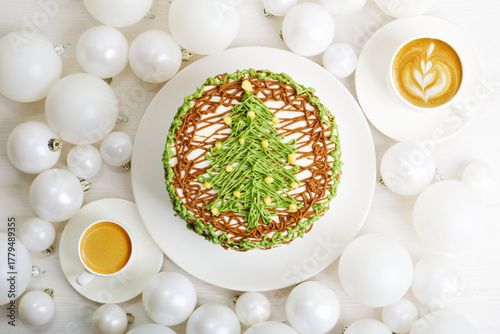 Homemade cake decorated with christmas tree, two cups of coffee and Christmas balls on white wooden table. Top view.