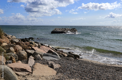 Fototapeta Naklejka Na Ścianę i Meble -  Landscape photo with a view of the Baltic Sea coast with large rocks and pebbles and a stone in the sea with birds sitting on it at Cape Grenen, in Skagen, northern Denmark