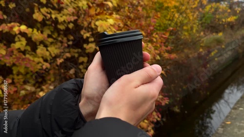 A black glass with a hot drink on the tipple against the background of yellow autumn trees.
