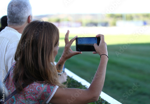 Mujer grabando y fotografiando con teléfono móvil al aire libre en el hipódromo