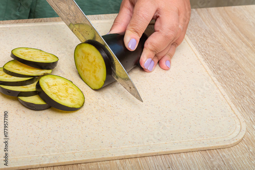 Fresh young eggplants are cut with a knife on a wooden board on the table