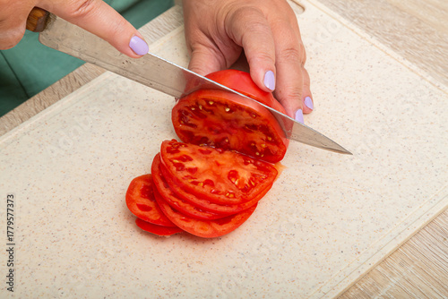 Red tomatoes are cut with a knife on a wooden board on the table