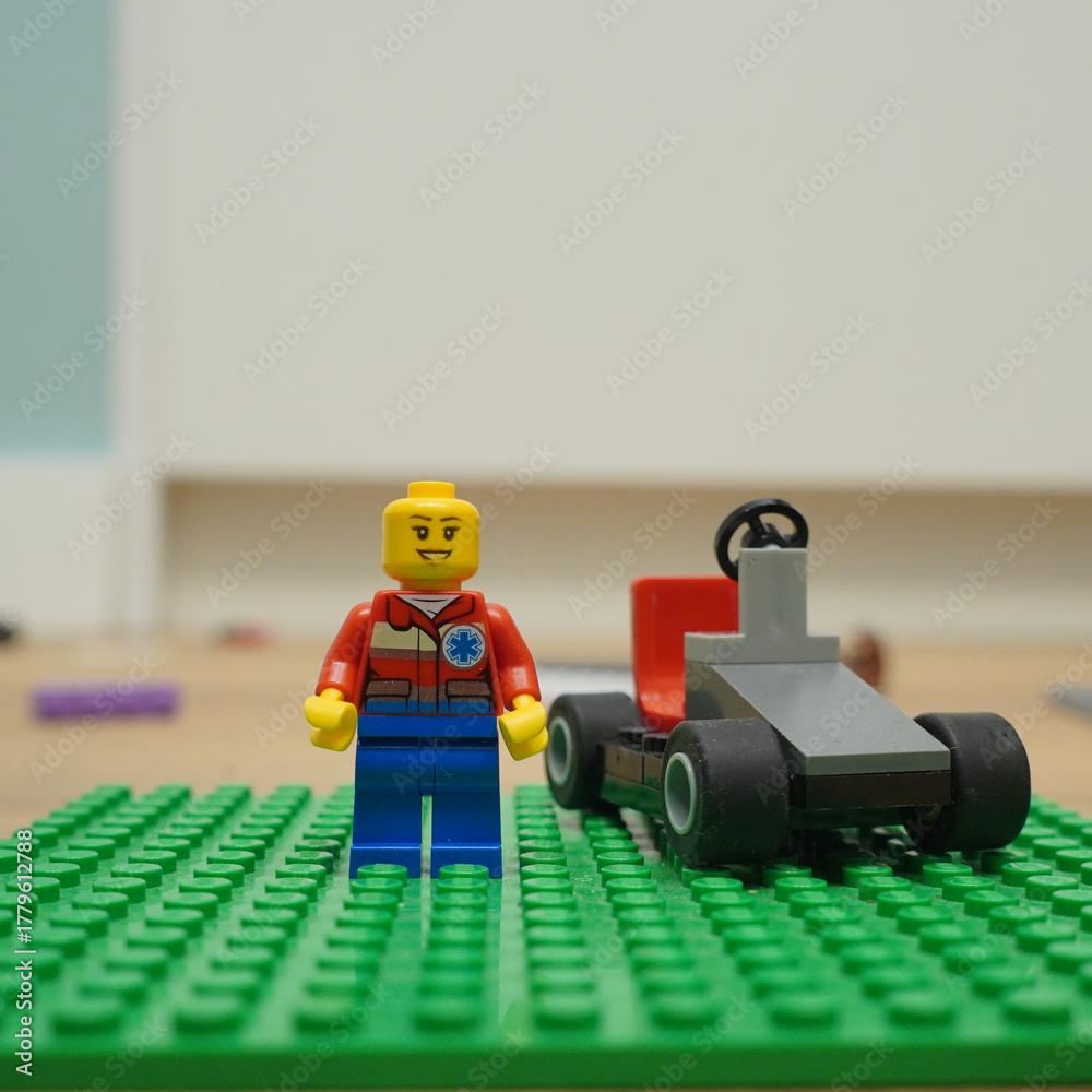 Naklejka premium Lego minifigure stands next to a small race car on a green baseplate