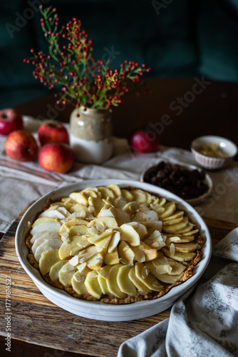 Unbaked homemade apple pie decorated with crust in baking form on rustic kitchen.