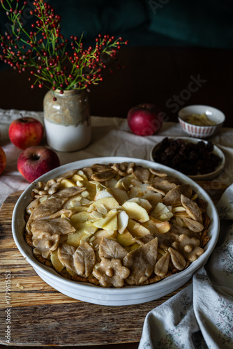 Unbaked homemade apple pie decorated with crust in baking form on rustic kitchen.