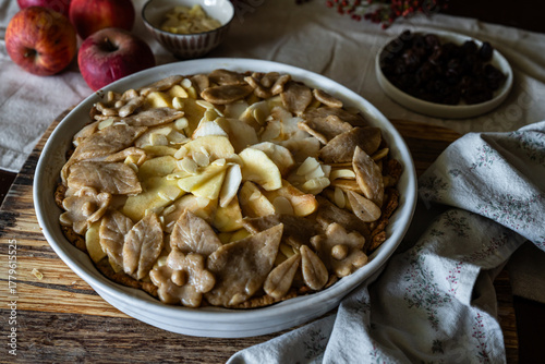 Unbaked homemade apple pie decorated with crust in baking form on rustic kitchen.