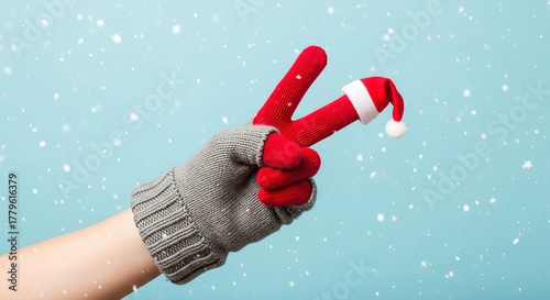 Hand in glove showing peace sign with Santa hat in snow. A whimsical, joyful gesture for winter. Holiday spirit, festive mood, joyful season.