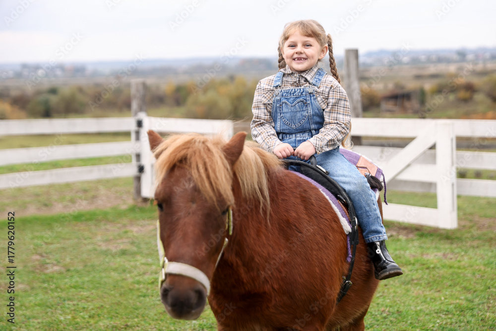 Fototapeta premium Equine assisted therapy. Little girl riding beautiful pony outdoors. Lovely domesticated pet