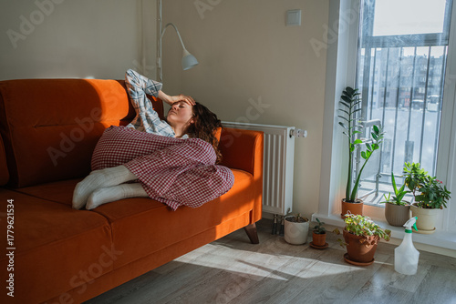 Young pregnant woman with toxicosis resting on a sofa under a blanket, looking unwell and fatigued from nausea and headache during early pregnancy at home