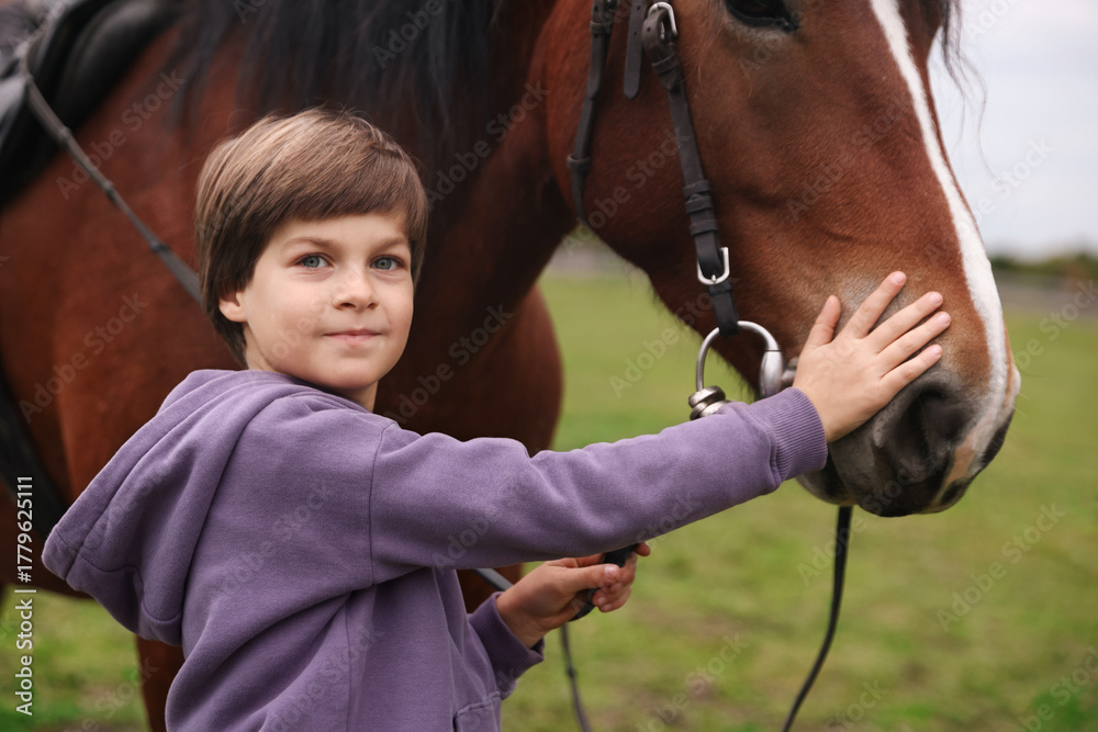 Obraz premium Equine assisted therapy. Little boy stroking beautiful horse in countryside. Lovely domesticated pet