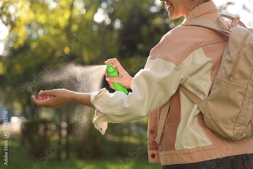 Woman spraying tick repellent onto hand in park, closeup