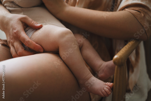 A mother sits in a wooden chair, gently breastfeeding her baby in a warm and softly lit room. Sunlight filters through the curtains, creating a peaceful atmosphere.
