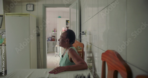Cuadro en lienzo Elderly woman sitting alone at a dining table in a simple kitchen, staring thoug