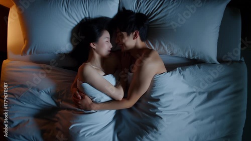 couple cuddling in bed at night, embracing under soft blue bedding, peaceful sleep with warm bedside glow, intimacy and affection, top‑down overhead view in a cozy bedroom with pillows