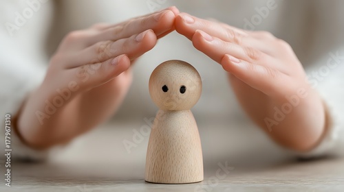 Protective hands hovering over wooden peg doll figurine, symbolizing care, support, and guardianship in mental health, family services, or childhood development.