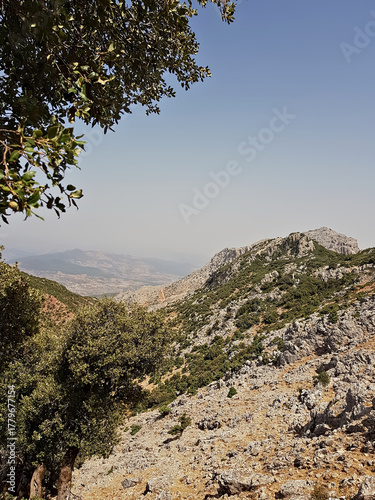 Ridgelines and rugged cliffs rise to reveal cliffs and hills far below in a sunlit landscape.