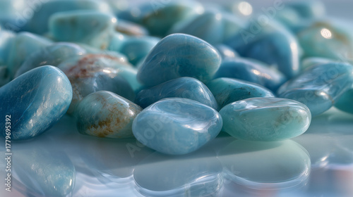 A collection of smooth, polished blue stones scattered on a reflective surface. The stones vary in size and shade, showcasing natural beauty and texture.