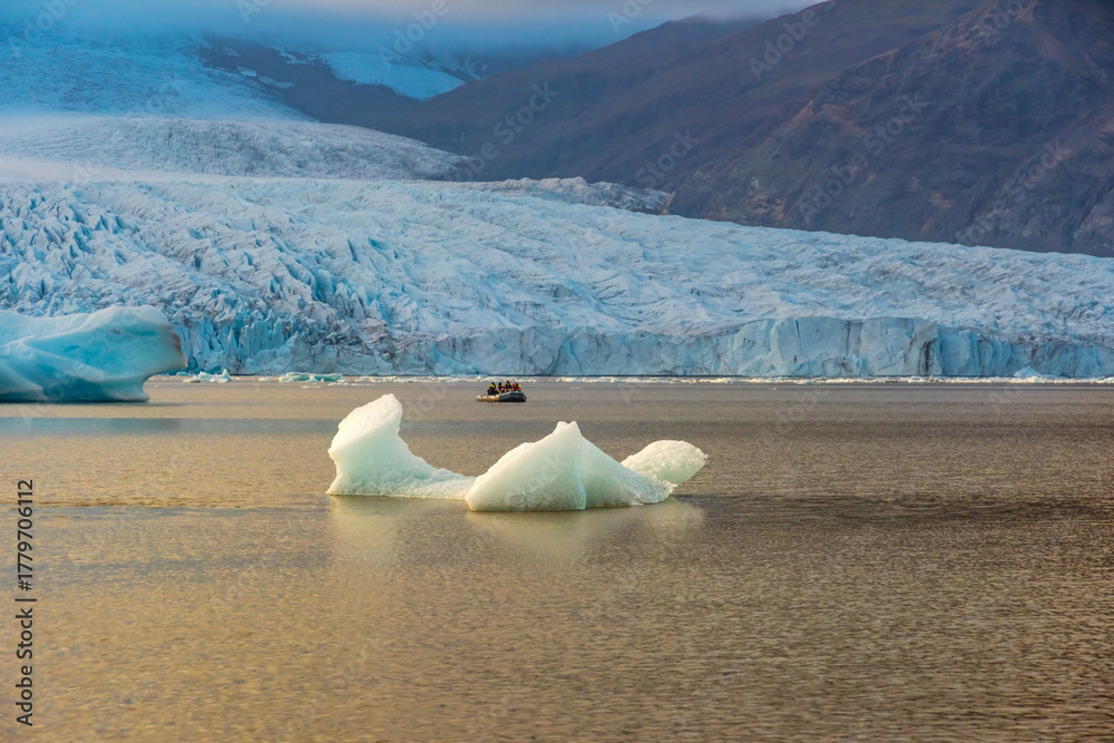 Obraz premium Fjallsarlon glacial lagoon showcases icebergs floating in calm waters, reflecting the soft twilight glow against the massive glacier backdrop. An iconic location in Iceland