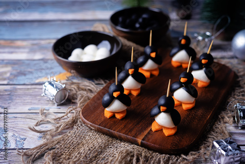 Mozzarella, carrots and black olives appetizer in the form of penguin on a cutboard for Christmas holidays