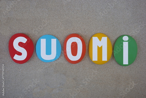 Suomi, Finnish name of Finland country, creative text composed with hand painted multi colored stone letters over beach sand