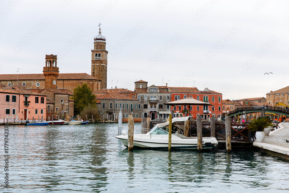 Fototapeta premium Murano, Italy - November 21, 2024: Scenic view of Murano Island with colorful buildings, boats on the water, and a historic bell tower, capturing the essence of Venetian charm and beauty