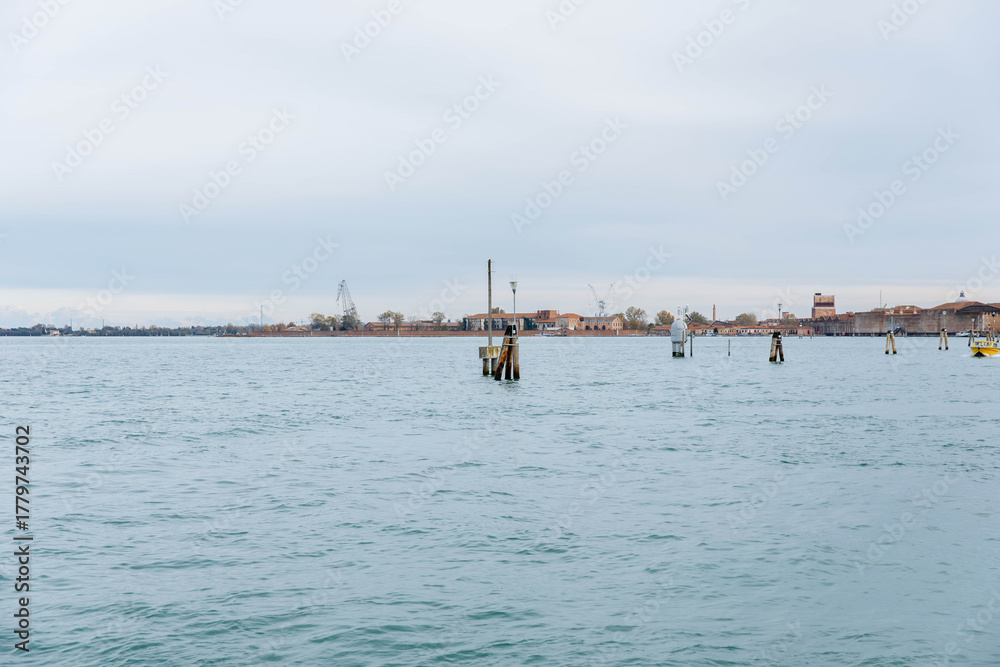 Fototapeta premium Murano, Italy - November 21, 2024: Scenic view of Murano Island with calm waters and distant buildings, showcasing the tranquil beauty of this famous Venetian destination