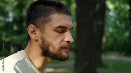 Close up view of young man eating cookie and chewing while sitting in green park on sunny day. 4k horizontal footage