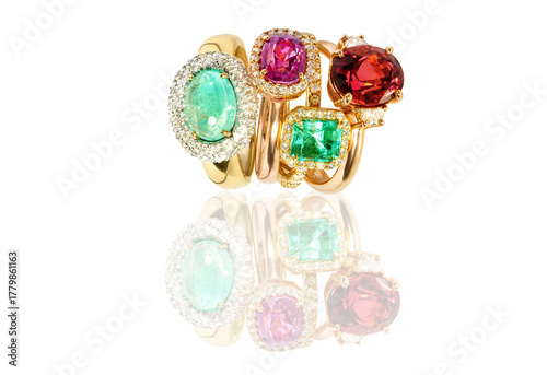 collection of elegant gold rings with large colorful gemstones, including emerald, ruby, and tourmaline. Luxury fine jewelry displayed on a reflective surface